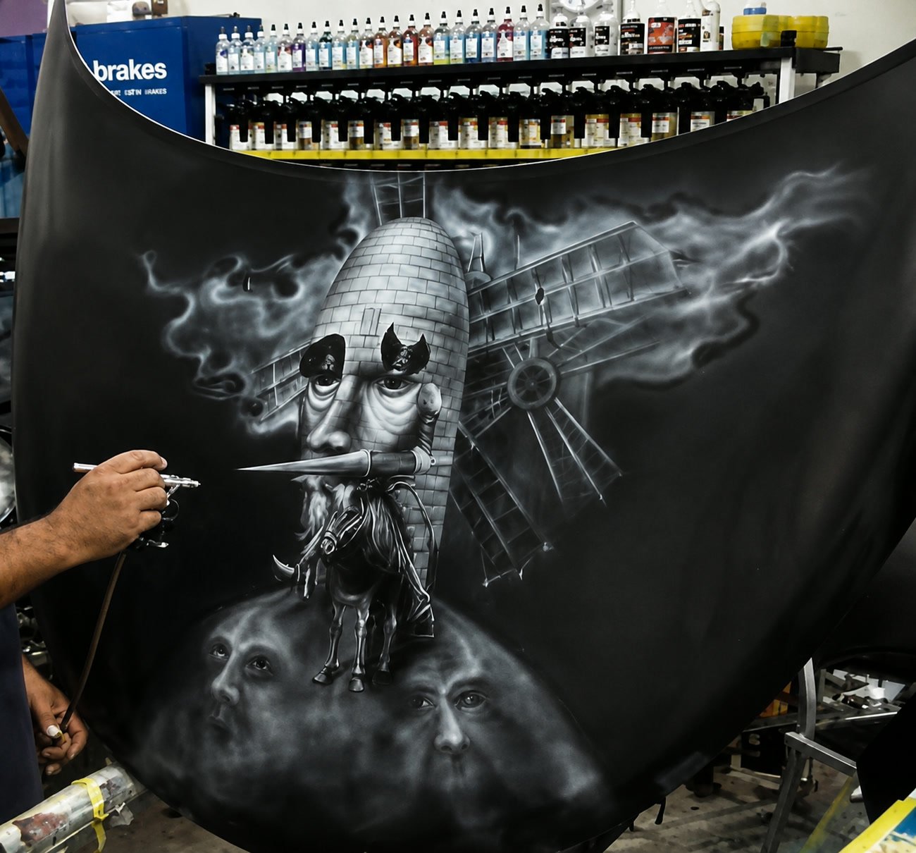 The artist working a grayscale mural onto a car hood with an airbrush