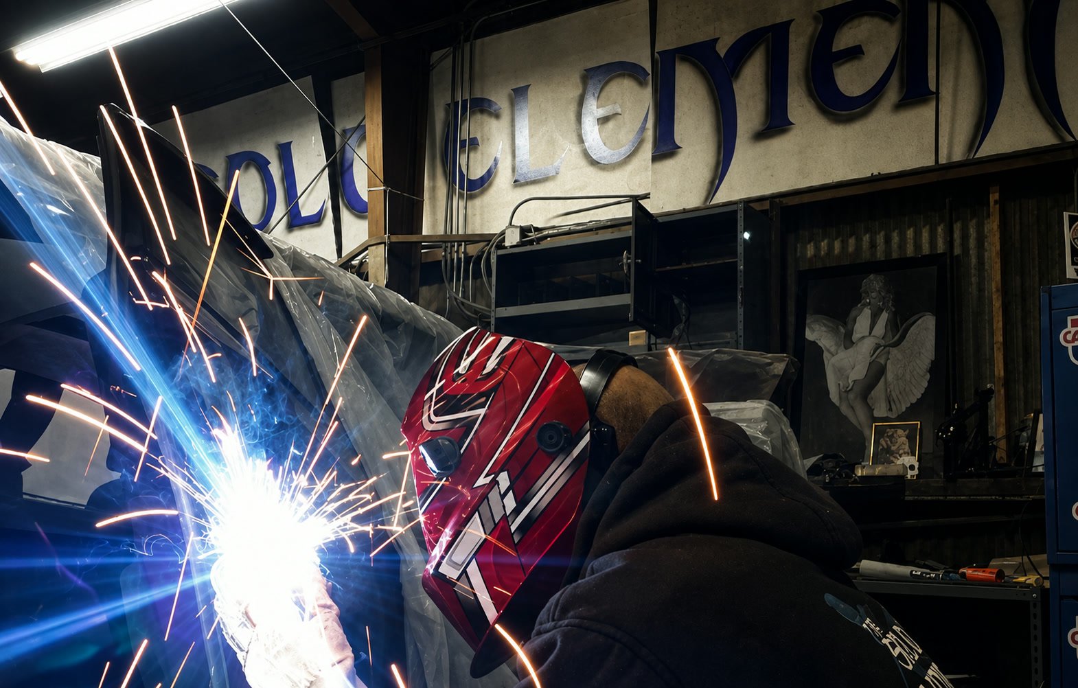 A fabricator welding, sparks flying, under the Solo Element sign inside the shop