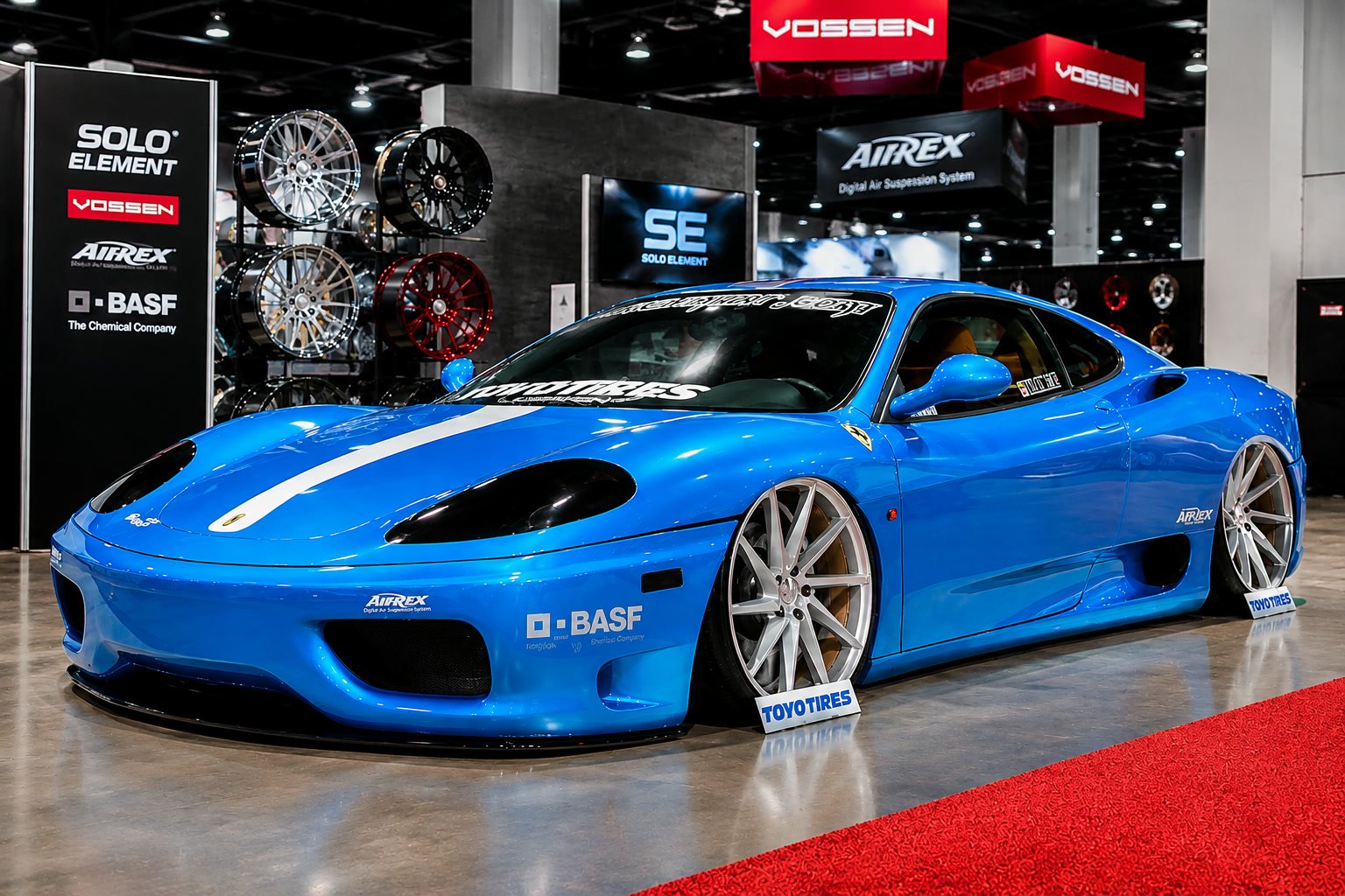 Blue wide-body Ferrari 360 Modena on silver wheels at a show stand