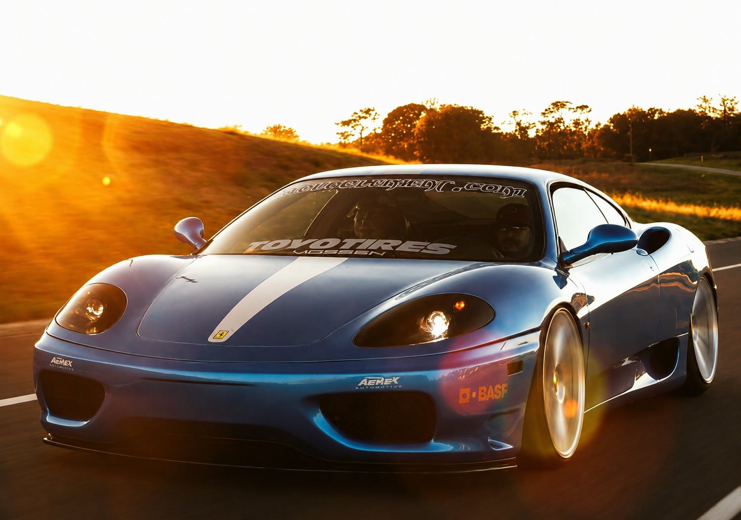 Blue Ferrari 360 Modena driving into a low sun