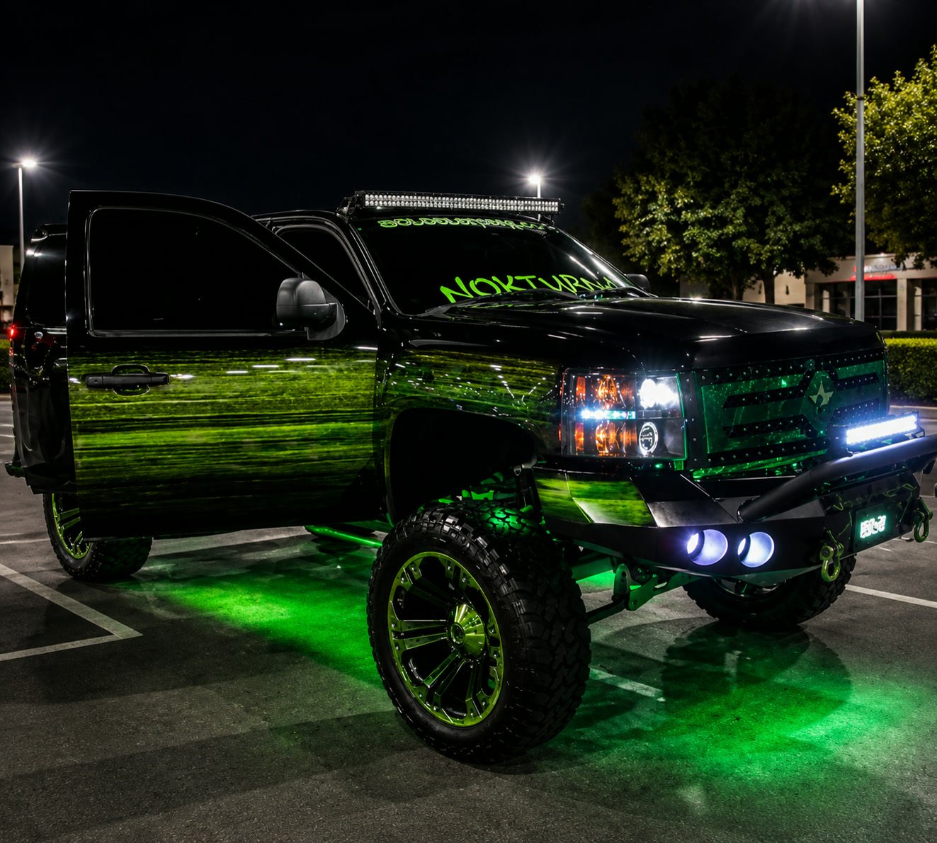 Lifted black Chevrolet Silverado with green paint effects and underglow at night
